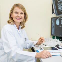 Portrait of happy female doctor sitting at examination room. Mature surgeon with CT scan reports. She is in hospital.